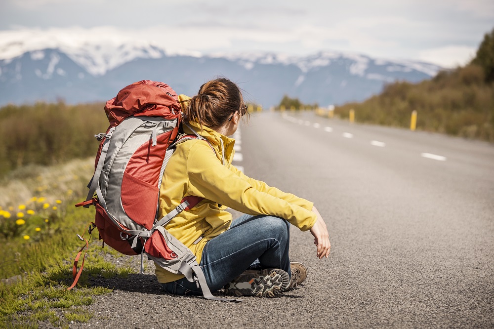 mulher com mochila sentada na beira da estrada com montanhas ao fundo